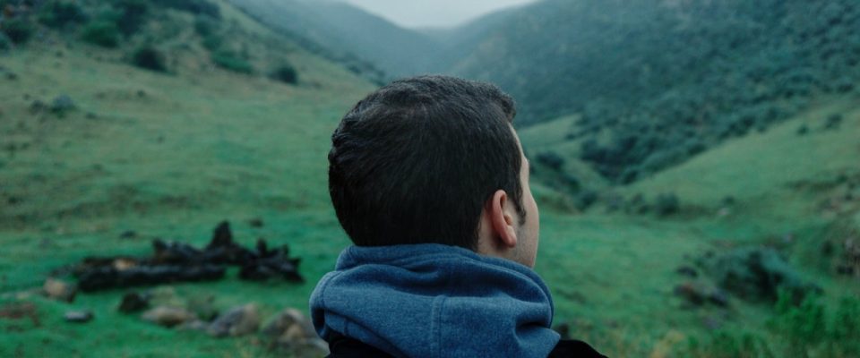 Man looking out over a field and mountains